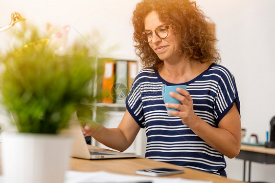 随意的设计师坐着中年妇女在办公室喝热咖啡的中年妇女图片