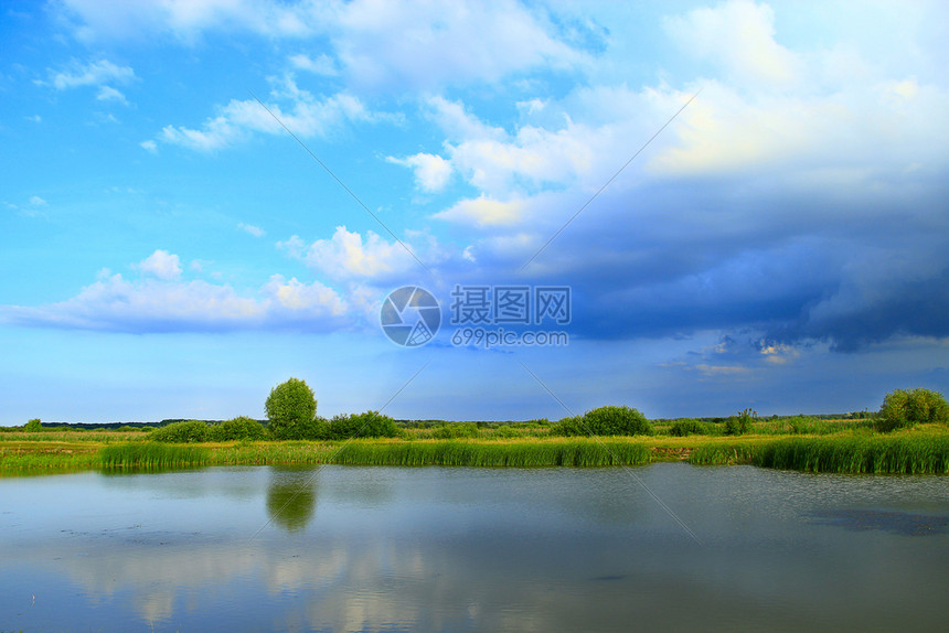 水在美丽的自然风景中奔流而出池塘和云彩湖面与甘蔗和大云环绕的湖面林木在美丽的自然景观中横冲直撞夏天芦苇图片