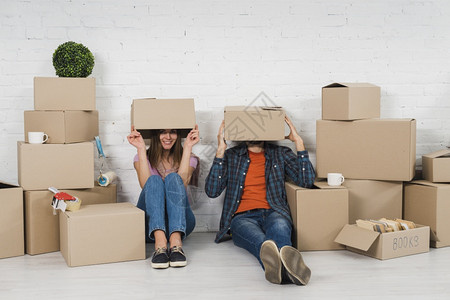 幸福坐着爱年轻夫妇把面容藏起来坐在纸板箱中他们的新房子里图片