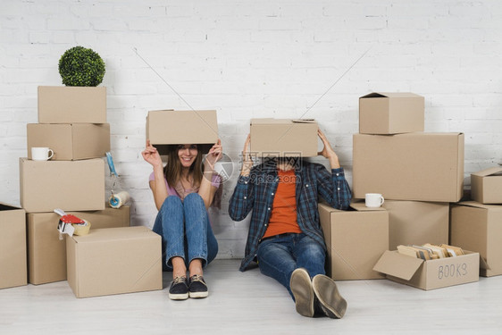 幸福坐着爱年轻夫妇把面容藏起来坐在纸板箱中他们的新房子里图片