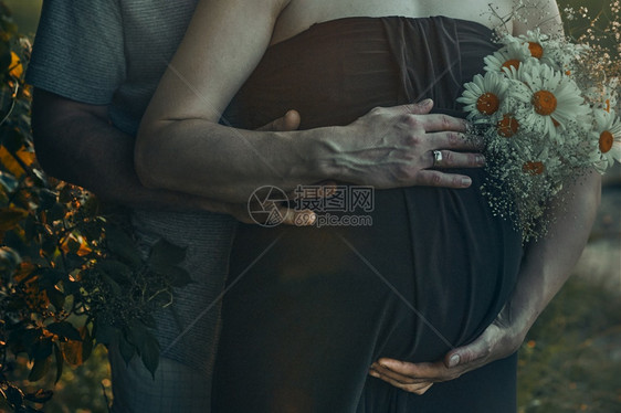 怀孕妇女及其丈夫拥抱肚子站在户外被自然期望母概念包围着的孕妇和丈夫围抱着肚子母亲幸福预期图片