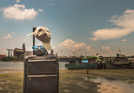 水娱乐河背景在PierSkRiver和船上的SpierSkRiver和船只上装有Cap相机和太阳眼镜的手提箱或行李袋暑假旅设计概图片