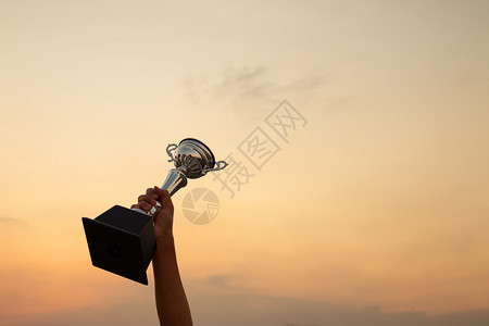 竞赛杯锦标胜利概念手握着日落天空背景的战利品图片