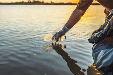 在日落的河边将垃圾塑料瓶装在黑袋中的志愿者目回收生态图片