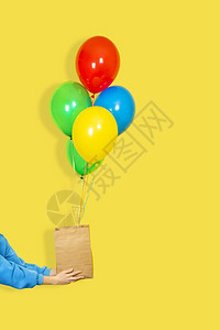 黄色的惊喜一种女手拿着纸袋和一束气球销售或呈现概念绿色红黄和蓝气球棕纸袋和手在黄背景上隔开女手拿着纸袋和一束气球绿色棕纸袋和黄背图片