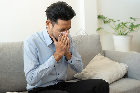 坐在沙发上感冒擦鼻涕的男性图片