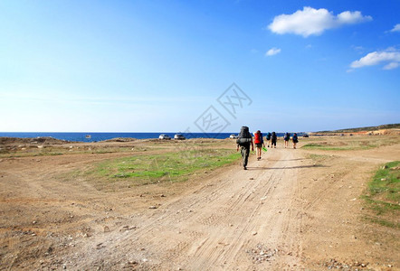 徒步旅行一群背包车在阳光灿烂的天空背景下沿海边一条沙路行走的背包车夏天自由图片