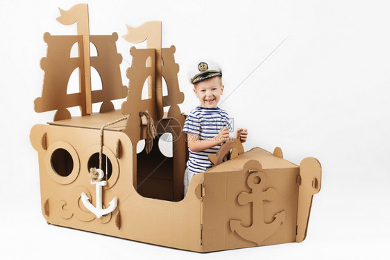 条小男孩玩纸板船白色背景快乐的孩子可爱打扮成水手童年幻想象力带子海洋图片