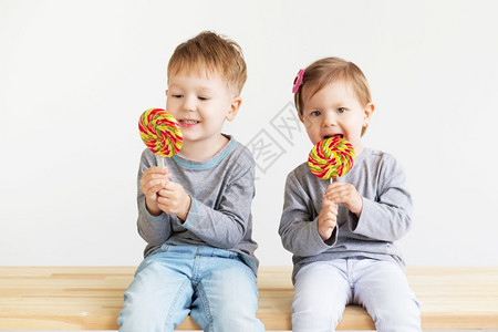 可爱的坐着孩子们吃棒糖快乐的孩子带着一大颗糖果快乐的小孩子肖像一个快乐的小孩子男和女美丽的子在白色背景下愉快图片