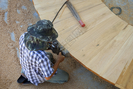 座位亚洲木匠使用电平板在户外车间用亚洲木制长椅刮剃边缘的观察意见装修锯末图片