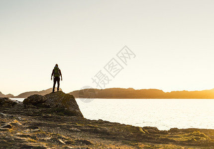 一种拍摄个享受日落时海岸风景的男人滩岩石图片