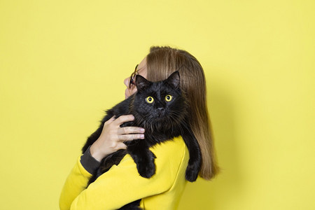 猫咪穿黄色连衣裙的女孩抱着她心爱的黄色背景上眼睛毛茸的黑猫宠物护理概念穿着黄色连衣裙的女孩抱着她心爱的黄色背景上眼睛毛茸的黑猫宠图片