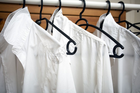 出口洗衣店一排白色棉挂在架上的黑色特写白色衬衫干净和新一排白色棉衣挂在架上的黑色特写白色衬衫织物图片