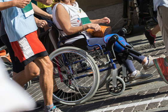 男人竞赛种族在马拉松比赛期间在跑步者的帮助下坐在运动轮椅上的残疾运动员在马拉松比赛期间在跑步者的帮助下坐在运动轮椅上的残疾运动员图片
