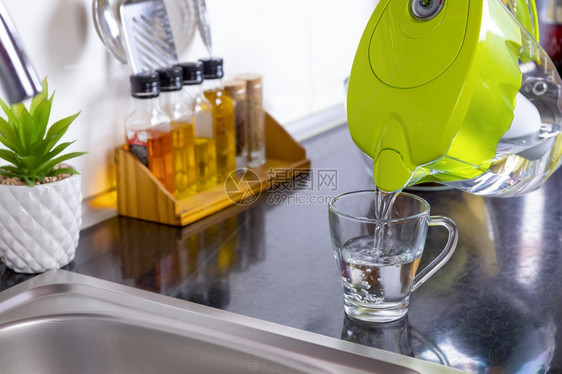 人们从厨房的过滤水壶中将的从厨房自来水净化和软抽倒入玻璃以为焦点新鲜的液体图片