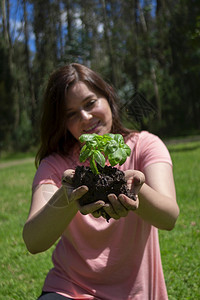 美丽的西班牙裔年轻女子在她的田间手上拿着一株小植物然后在早上被种植树木环绕的绿地上花园肖像农业图片