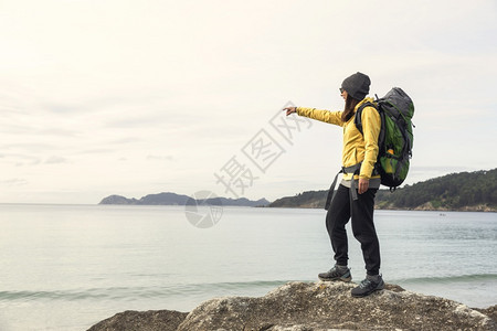 秋天探险家游客带着背包的女士享受着并指向美丽的海岸清晨风景图片