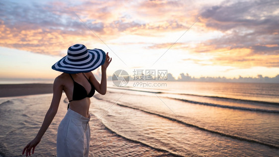 畅快积极的身穿比基尼和白色长裤的顶层比基尼女人在海滩上戴帽子背面日出或落美丽外部图片