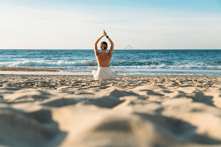 在海滩上披着毛巾的瑜伽姿势下坐着年轻女子的后视镜有意识运动一种图片