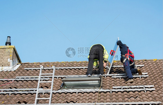 把太阳能电池板安装在屋顶上的工人图片