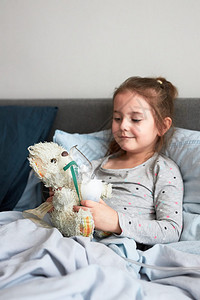 在床上的生病小女孩玩耍她的泰迪熊图片