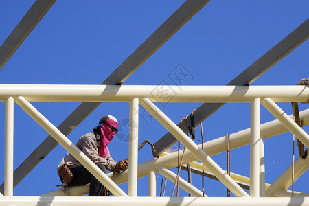 在职的电缆亚洲建筑工人在阳光明日的蓝天背景下将金属焊接在楼顶结构屋上泰国图片