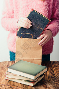 在书店把放进纸袋里的年轻女孩几本关于一个身穿粉红色毛衣和蓝牛仔裤垂直照片的木桌青少年女孩的书爱好木头阅读图片