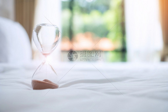 清晨阳光下躺在床上的沙漏流经玻璃灯泡测量穿越时间倒计最后期限生命和退休日常概念等情况窗户滴漏专业的图片