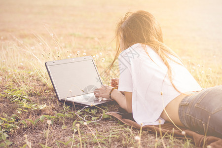 花园女孩躺在地上用笔记本电脑在公园里早晨阳光照耀在线的草地图片