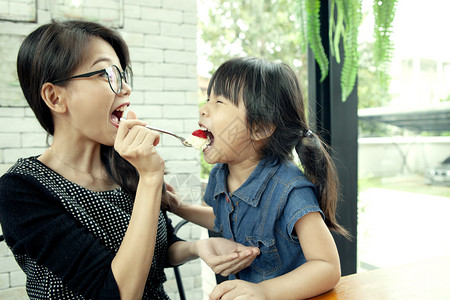 美味的勺子在家中客厅吃草莓蛋糕的亚洲女和儿漂亮的图片