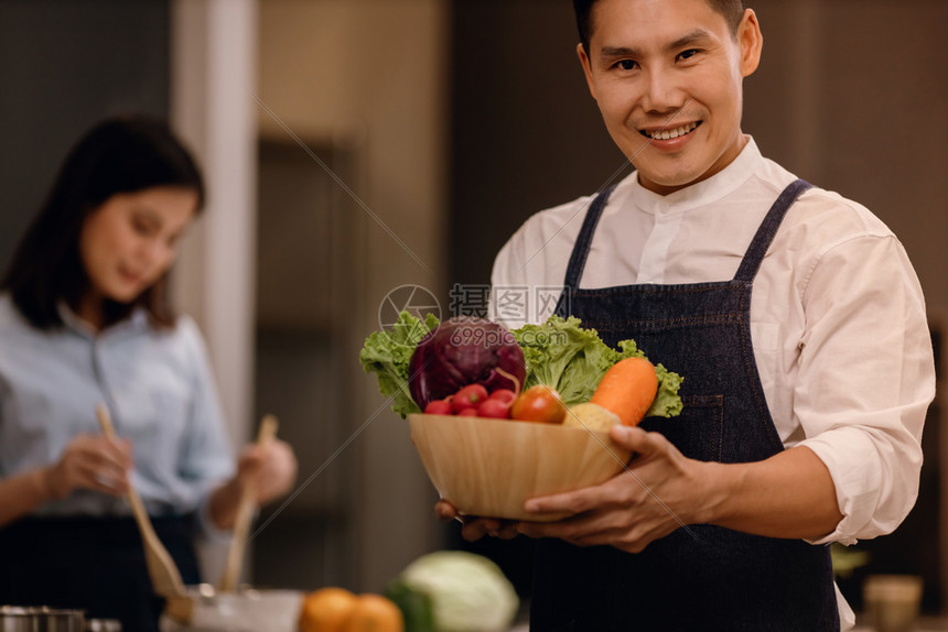 a笑人与一碗新鲜蔬菜起微笑为在现代厨房冷却的中吃食织女装物做准备将健康沙拉作为家庭健康生活方式概念烹饪的背景为了男厨师图片