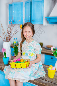 快乐的装饰可爱女孩拿着篮子和彩蛋在厨房煮饭为假日复活节可爱女孩做饭带彩蛋的篮子象征图片