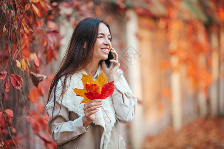 户外自然美丽的女人在秋天公园里通过电话在秋天的落叶下美丽女人在秋天公园里落叶下时尚图片