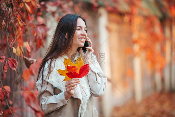 户外自然美丽的女人在秋天公园里通过电话在秋天的落叶下美丽女人在秋天公园里落叶下时尚图片