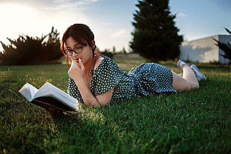 白种人松弛女身着古老的代旧礼服天主教女孩在日落时读了一本关于草坪的书图片