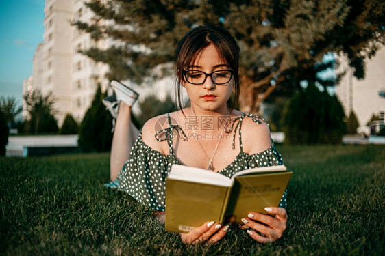 松弛漂亮的身着古老代旧礼服天主教女孩在日落时读了一本关于草坪的书小说图片
