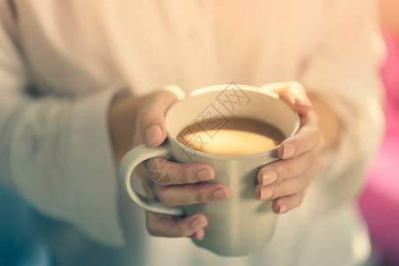 妇女双手在清晨阳光下握着热咖啡或茶杯女士温暖的放松图片