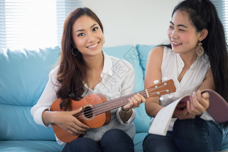 两个Asiia女人玩着乐于乌鲁莱拉在家里笑着享受放松时光女士声学艺术图片