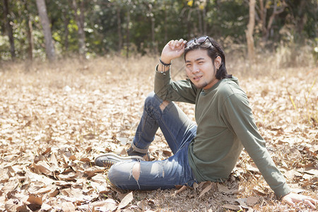 微笑乐趣坐在干叶田上面带笑脸的亚洲年轻男子成人图片