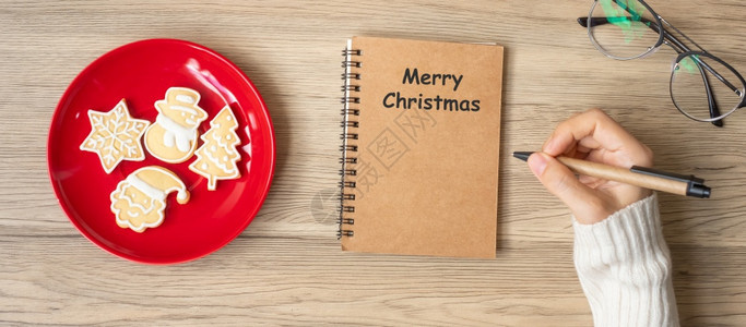 快乐的复制空间妇女手写笔记本在表格Xmas新年快乐目标决议清单战略和计划概念上用圣诞饼干写字棕色的图片