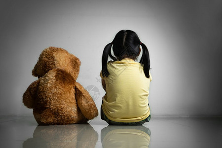 自闭症坐着有泰迪熊的小女孩坐在空房间里的地板上精神和沮丧的家庭概念后视墙图片