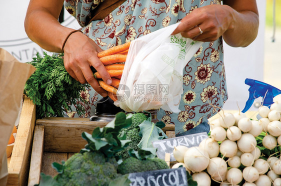 新鲜的快乐妇女在农民市场亲近手购买胡萝卜当地的图片