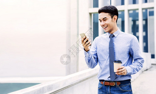 在城市现代生活方式中使用移动电话的年轻亚洲商人微笑男肖像手在咖啡杯上观看智能手机并举行咖啡杯亚洲人城市的视频图片