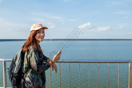 背着明亮包的亚洲女在背景山上的旅游行者背后看使用智能手机的女从后面看图景快乐的亚洲人太阳图片