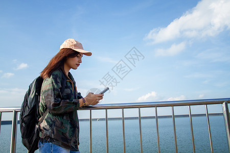 一种背着明亮包的亚洲女在背景山上的旅游行者背后看使用智能手机的女从后面看图景自然背包客图片