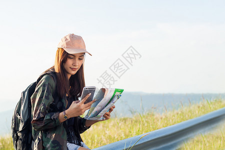 摄影师小样吸引人的背着明亮包亚洲女在背景山上的旅游行者背后看使用智能手机的女从后面看图景图片