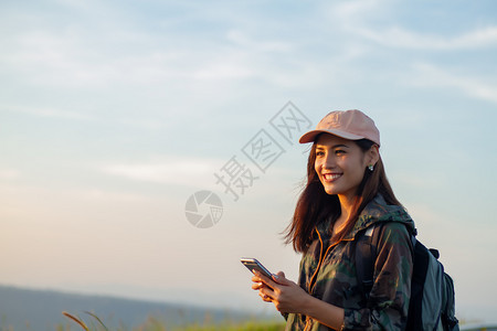 景观年轻的背着明亮包亚洲女在背景山上的旅游行者背后看使用智能手机的女从后面看图景假期图片