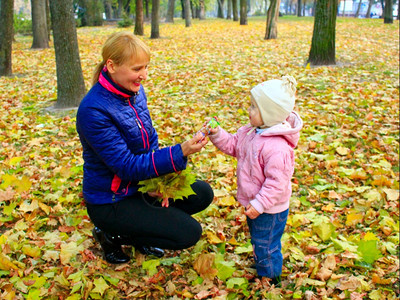 女人在秋天的公园里给女儿一个糖果人在秋天的公园里给她小女儿一个糖果美丽的种女士图片