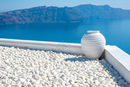蓝色的鹅卵石阳台圣托里尼白石块和花瓶与岩岛屿白瓦塞和桑尼群岛的海景图片