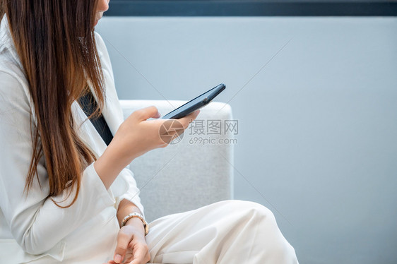女商人穿白衣乐于在人背景下玩手机一种网络高兴的图片